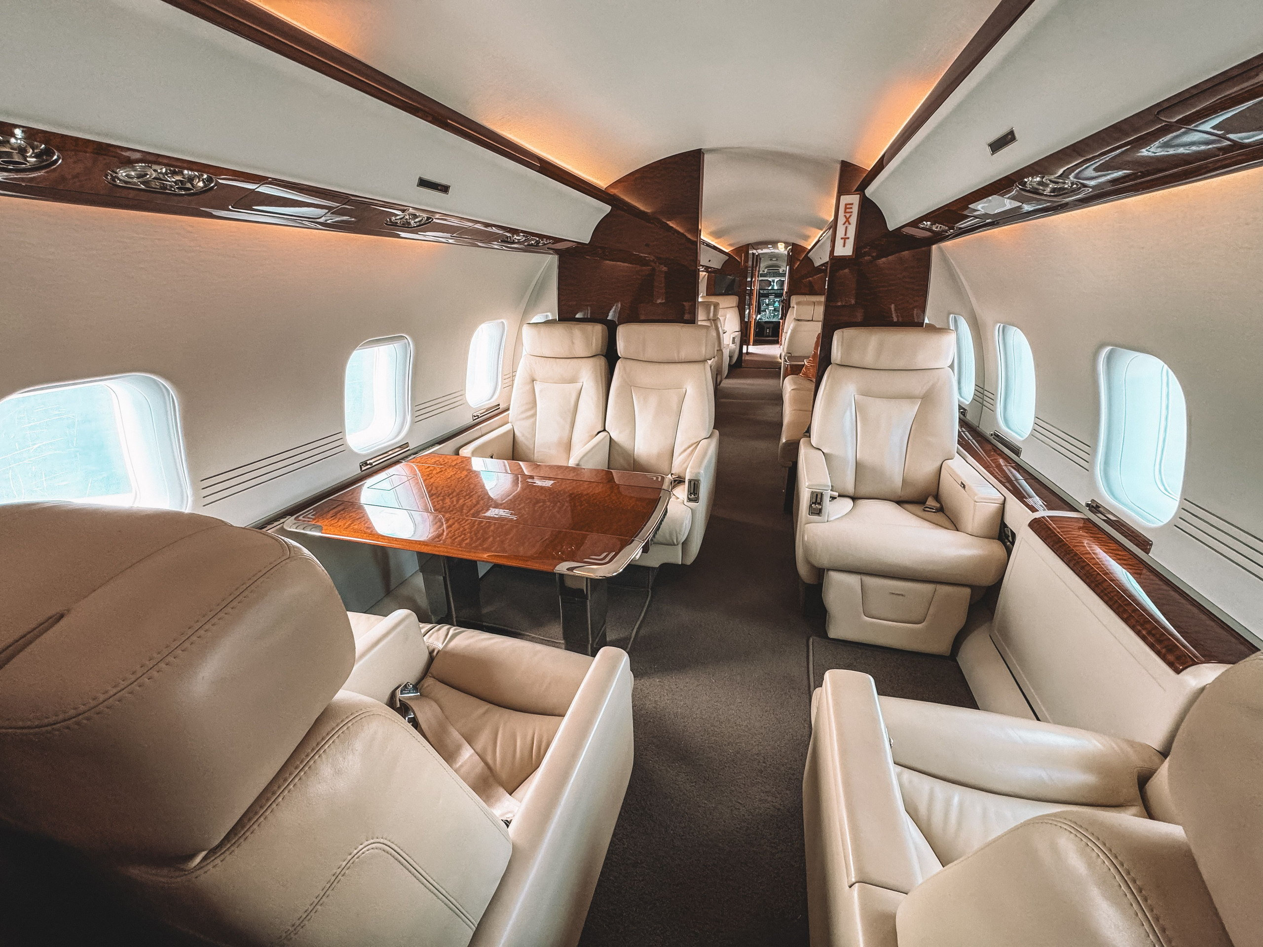 Business jet cabin interior with cream leather seats and a polished wood table